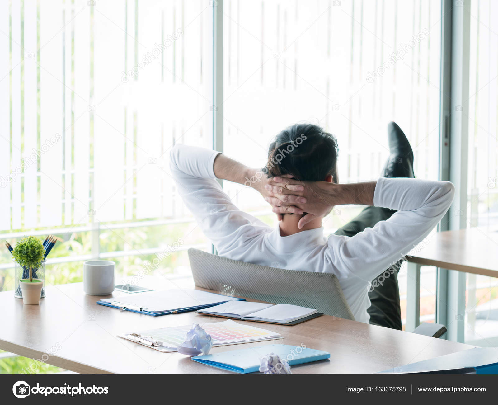 Businessman sitting in office with feet up on desk - Stock Photo