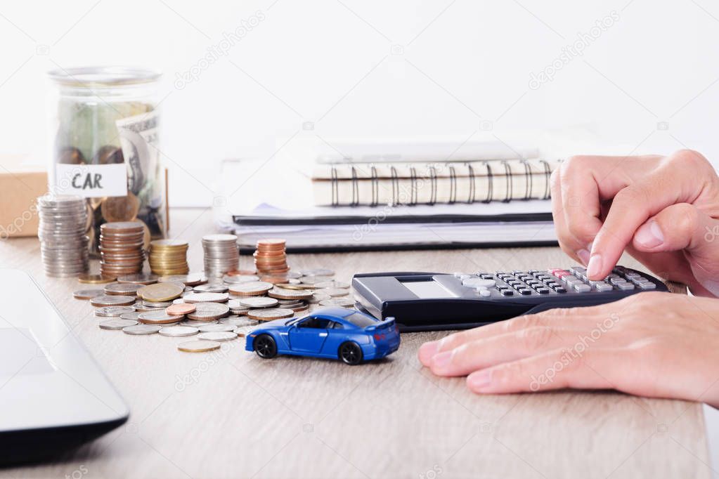 Man using calculator with car toy and coin stack for insurance loan or Saving for buying car concept