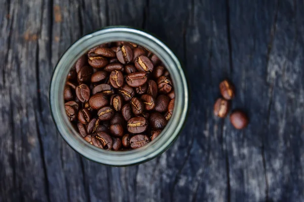 Boabe de cafea prăjite în recipiente de sticlă pe fundal vechi de masă din lemn, vedere deasupra capului cu spațiu de copiere — Fotografie, imagine de stoc