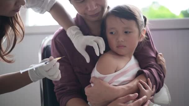 Bambino piccolo che fa l'iniezione, medico di primo piano che inietta la vaccinazione al braccio della bambina asiatica, con il padre che abbraccia il bambino, per non dimenarsi durante l'iniezione della vaccinazione — Video Stock