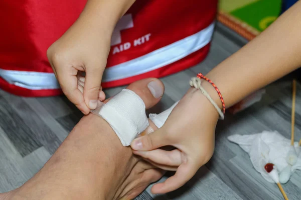 Child's hand is giving first aid to father injured at home at night time — 스톡 사진