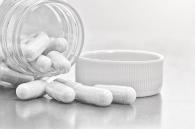 Yakından şişeden çıkan bitkisel ilaçların beyaz kapsülleri.