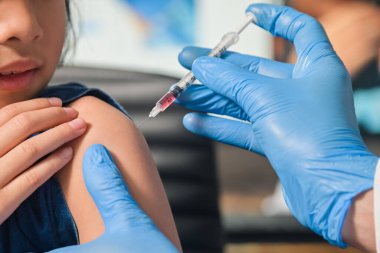 Küçük çocuk iğne yaptırıyor, doktor Asyalı küçük kız aşısının koluna aşı enjekte ediyor. Hastane sağlığı ve tıbbi konsepti. 4-6 yaşlarında.