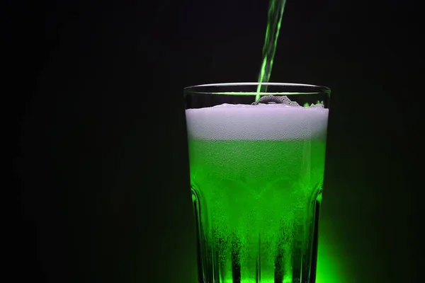 ビールグラスにグリーンビールを注ぐ夜の暗い背景にStパトリックの一日パーティーであなたの広告デザインの背景とコピースペース — ストック写真