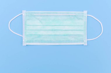 Tıbbi yüz maskesi, mavi arka planda tıbbi koruyucu maske. Tek kullanımlık yüz maskesi ağız ve burnu kapatır. Sağlık hizmetlerini ve tıbbi konsepti koru.
