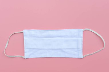 Pembe arka planda korunmak için beyaz kumaş yüz maskesi. Ağız ve burnu kapamak için açık hava aktivitesi, hastalık veya hava kirliliği sağlık ve tıbbi konsept.