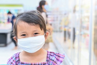 Küçük kızın kumaş maskesi var. Çocuk süpermarketten sonra annesiyle süpermarkete gittiğinde kendini Coronavirus 'tan koruyor. Salgından sonra açık hava aktivitesi için burnuna maske takmış bir çocuk..