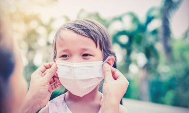 Anne, küçük kız için bez bir maske takıyor. Kendini Coronavirus 'tan koru. Çocuk evden ayrıldığında anne, dışarıda güvenlik aktivitesi, hastalık ya da hava kirliliği için burnuna maske takıyor..