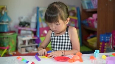 Asyalı küçük kız çocuklar oyuncakta kil kalıbı oynuyorlar ve oyuncak köşesine yaslanıyorlar Cumartesi sabahı kalkınmaya yaslanıyorlar.