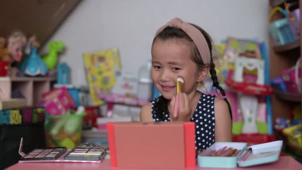 Asyalı küçük kız makyaj yapıyor ve yüzünü boyuyor. Mutlu çocuk evde annesinin kozmetik ürünleriyle deneyler yapıyor. — Stok video
