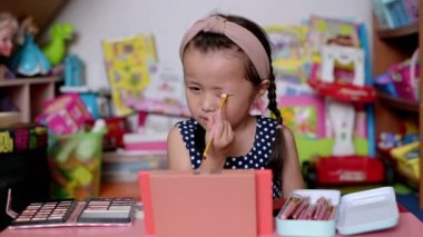 Çocuk makyajı, Asyalı küçük kız göz makyajı yapıyor ve yüzünü boyuyor. Mutlu çocuk evde annesinin kozmetik ürünleriyle deneyler yapıyor.