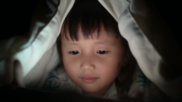 Little Girl are watching video in mobile phone on bed at night time light flashes reflected from the screen,children using games with addiction and cartoon concepts — Stock Video