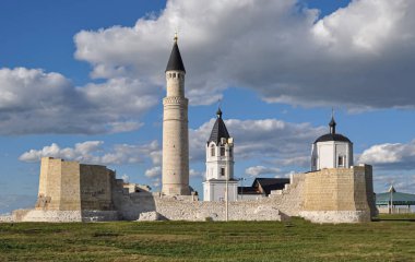 A view of the medieval Muslim minaret and the Christian Orthodox Cathedral, standing close to each other, behind an old brick wall with the skeletons of towers along the edges on a sunny summer day
