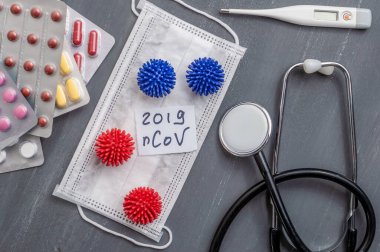 Medical face mask, stethoscope, pills and digital thermometer with inscription Wuhan coronavirus 2019-nCoV on the gray table background. Novel coronavirus 2019-nCoV concept.
