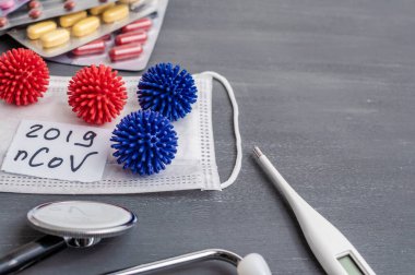 Medical face mask, stethoscope, pills and digital thermometer with inscription Wuhan coronavirus 2019-nCoV on the gray table background. Novel coronavirus 2019-nCoV concept.
