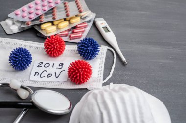 Medical face mask, stethoscope, pills and digital thermometer with inscription Wuhan coronavirus 2019-nCoV on the gray table background. Novel coronavirus 2019-nCoV concept.