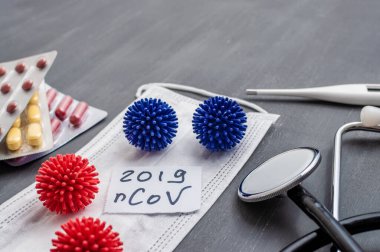 Medical face mask, stethoscope, pills and digital thermometer with inscription Wuhan coronavirus 2019-nCoV on the gray table background. Novel coronavirus 2019-nCoV concept.