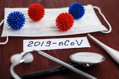 Medical face mask, sthetoscope and digital thermometer with inscription Wuhan coronavirus 2019-nCoV on the brown table background. Novel coronavirus 2019-nCoV concept.