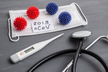 Medical face mask, stethoscope and digital thermometer with inscription Wuhan coronavirus 2019-nCoV on the gray table background. Novel coronavirus 2019-nCoV concept.