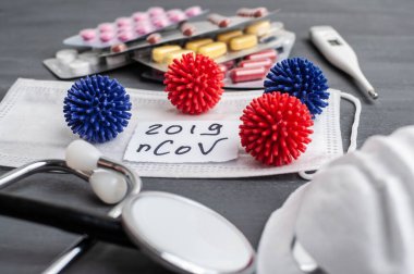 Medical face mask, stethoscope, pills and digital thermometer with inscription Wuhan coronavirus 2019-nCoV on the gray table background. Novel coronavirus 2019-nCoV concept.