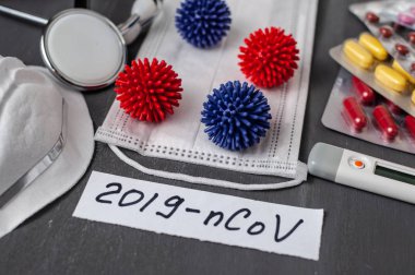 Medical face mask, stethoscope, pills and digital thermometer with inscription Wuhan coronavirus 2019-nCoV on the gray table background. Novel coronavirus 2019-nCoV concept.