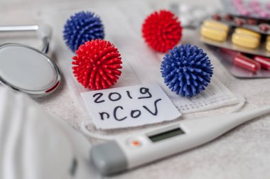 Medical face mask, stethoscope, pills and digital thermometer with inscription Wuhan coronavirus 2019-nCoV on the white table background. Novel coronavirus 2019-nCoV concept.