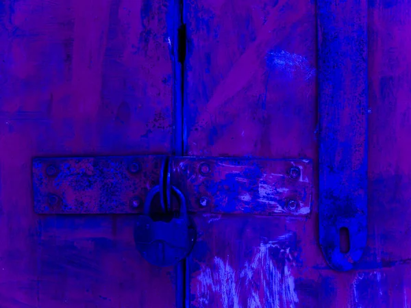 An old rusty iron gate locked with a large padlock and painted deep blue and purple in large spots