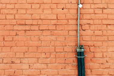 Kırmızı tuğladan bir duvara bağlanmış plastik ve metal koruyucu bir kablo.