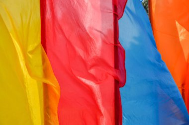 Güneşli, rüzgarlı bir günde bayrak direkleri üzerinde parlak, çok renkli dikey bayraklar dalgalanıyor. Fotoğraf kapanışı