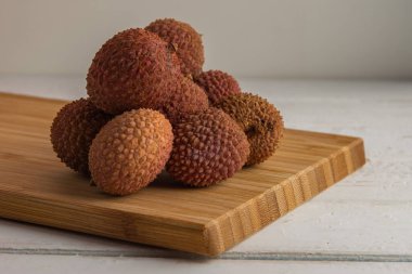 ripe lychee fruits lying on a bamboo board on a white wooden table