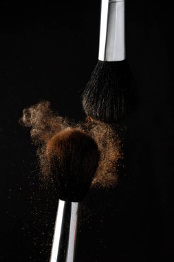 flying cloud of powder after the collision of two makeup brushes on a black background