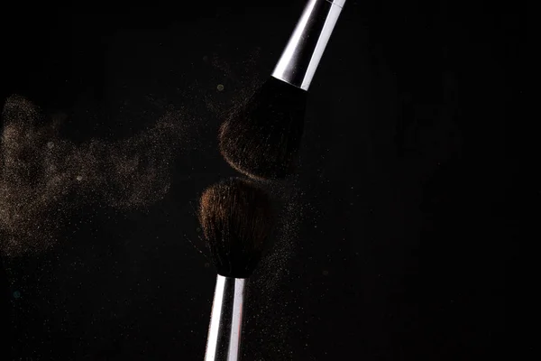 flying cloud of powder after the collision of two makeup brushes on a black background