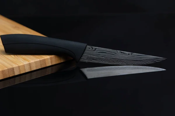 刀刃上刻有的刀和放在竹子上的黑色玻璃桌上的黑色把手 — 图库照片