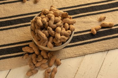 Beyaz seramik bir kasede bez bir masa örtüsü ve beyaz ahşap bir masa üzerinde kabuklu fıstıklar.