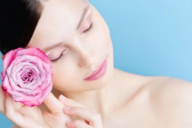 Mavi bir arka plan üzerinde pembe bir gül ile güzel bir esmer kız portresi