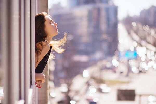 Photo of young beautiful happy smiling girl with long hair near the window. Sunny day. City lifestyle.