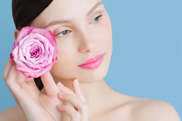 Porträtt av en vacker brunett tjej med en rosa ros på en blå bakgrund — Stockfoto