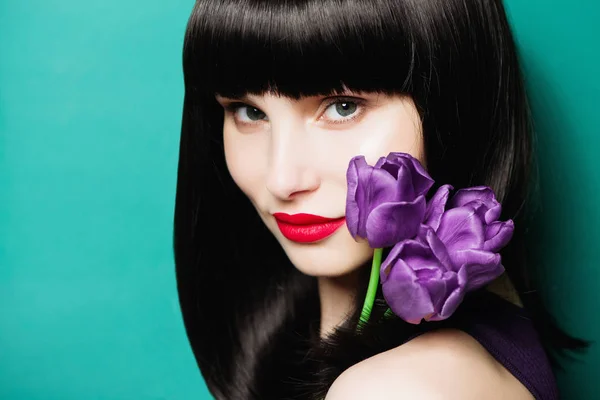 Portréja egy szép barna lány, egy lila tulipán, kék háttérrel — Stock Fotó