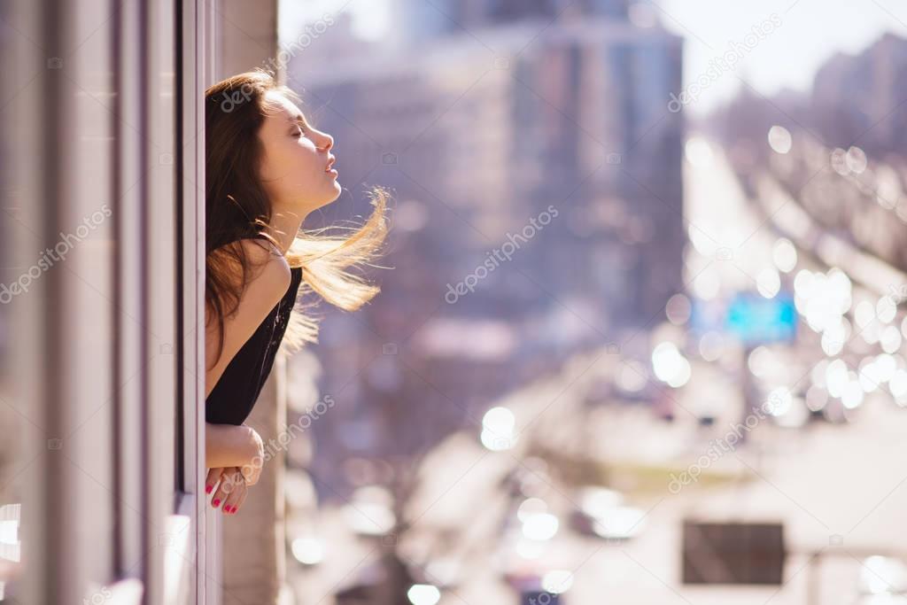 Photo of young beautiful happy smiling woman with long hair near the window. Sunny day. City lifestyle.