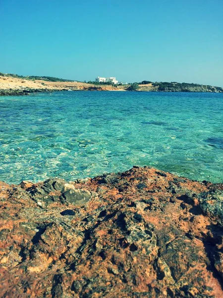 岩や砂とギリシャの海辺 背景に白い家 — ストック写真