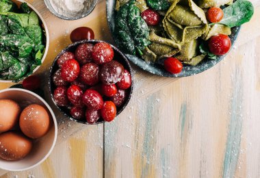 Eski ahşap bir masada domates, un, ıspanak, yumurta gibi taze malzemelerle çevrili ıspanaklı tortellini. Vejetaryen yemeği. kopyalama alanı