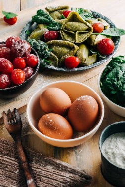 Eski ahşap bir masada domates, un, ıspanak, yumurta gibi taze malzemelerle çevrili ıspanaklı tortellini. Vejetaryen yemeği. kopyalama alanı