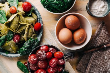 Eski ahşap bir masada domates, un, ıspanak, yumurta gibi taze malzemelerle çevrili ıspanaklı tortellini. Vejetaryen yemeği. kopyalama alanı
