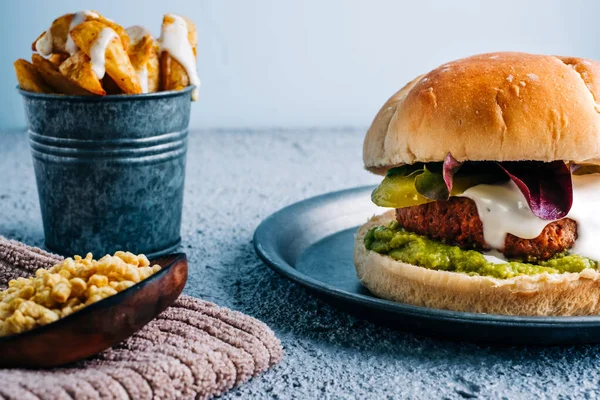 Soslu vejetaryen burger ve metal tabakta guacamole ve baharatlı patates kızartması.