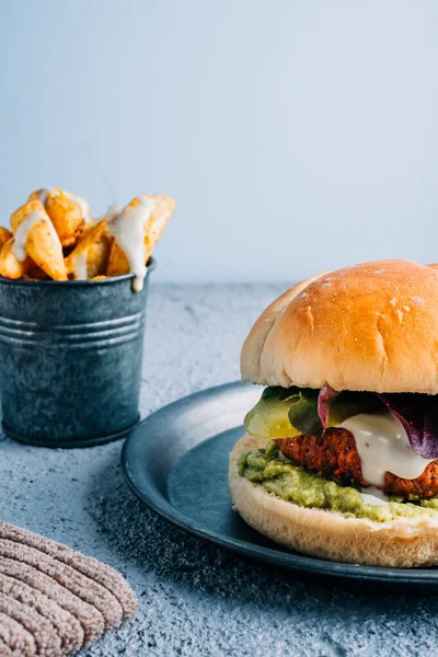 Soslu vejetaryen burger ve metal tabakta guacamole ve baharatlı patates kızartması.