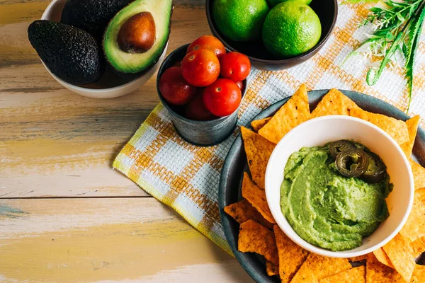 Antika ahşap masada taze malzemelerle birlikte nachos soslu guacamole kasesi. Uzayı kopyala Vejetaryen yemeği