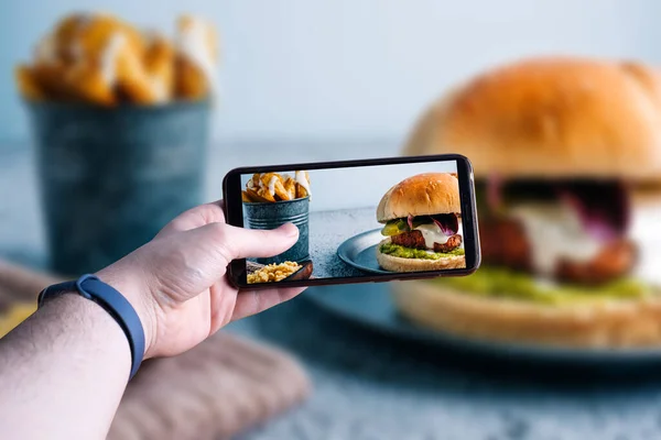 Hamburgerin fotoğrafını çeken akıllı telefonları kaldıran eller. Mesaj için yer var. Seçici odak