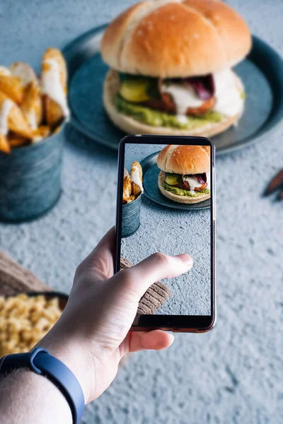 Hamburgerin fotoğrafını çeken akıllı telefonları kaldıran eller. Mesaj için yer var. Seçici odak