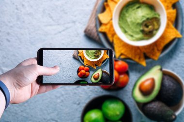 Akıllı telefonu kaldırıp guacamole soslu bir kasenin fotoğrafını çeken eller. Mesaj için yer var. Seçici odak