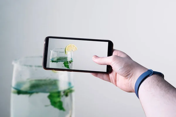 Akıllı telefonu kaldırıp ahşap bir masada limonlu mojitonun fotoğrafını çeken eller. Mesaj için yer var. Seçici odak